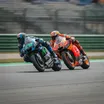 Two MotoGP motorcycles from different teams leaning at an extreme angle as they race side-by-side through a corner.