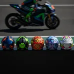 A row of five distinct and colourful MotoGP helmets sitting on a pit lane wall, symbolising the five different winners this season.