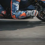 A close-up view of a MotoGP rider's arm and gloved hand, showing the extreme muscle tension required to control the bike.