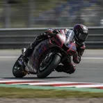 Marco Bezzecchi leans his Aprilia race bike at an extreme angle through a corner during a MotoGP race.