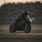 A MotoGP-style racing bike leans low through a corner at sunset, creating sparks as the rider's knee touches the track.