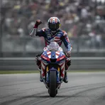 A MotoGP rider in Trackhouse Racing colours celebrates a victory on his motorcycle after a race.
