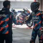 A rider and a team manager shaking hands in a MotoGP pit garage to signify a new contract agreement.